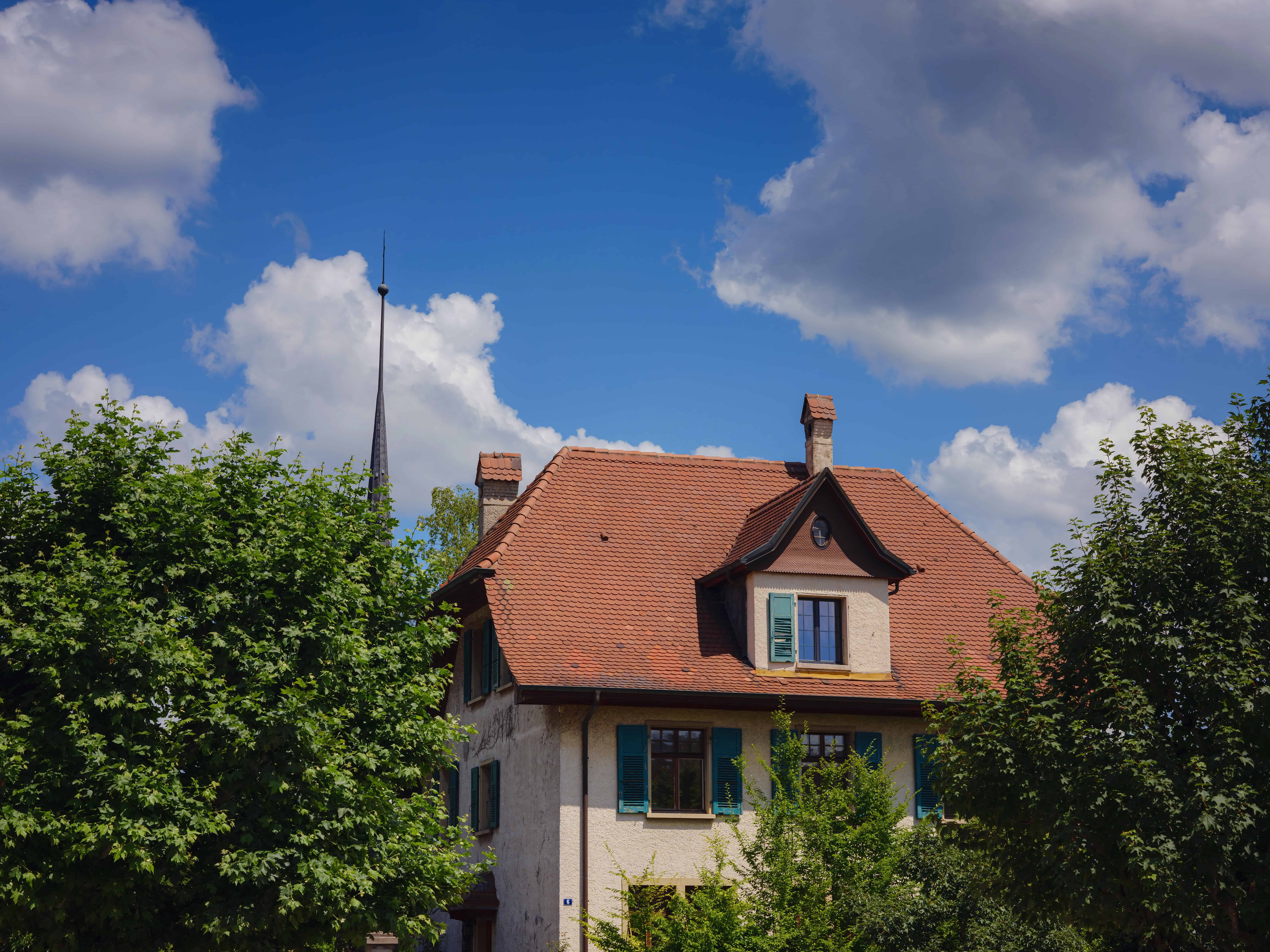 Maison en pierre, ciel bleu et arbres verdoyants.